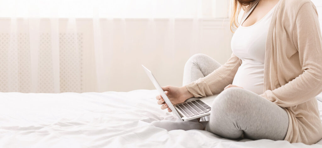 Woman on bed with computer, researching pregnancy and lupus
