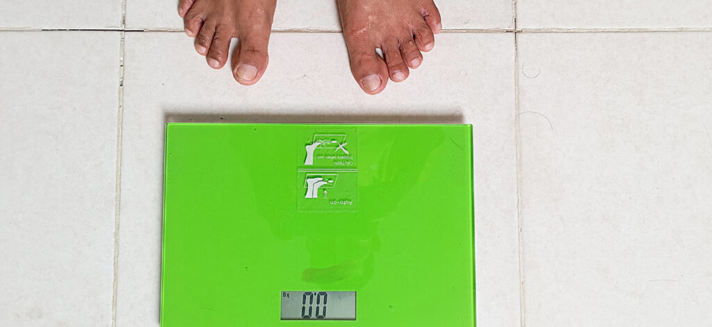 Person about to step on a scale to weight themself, looking at the causes of obesity
