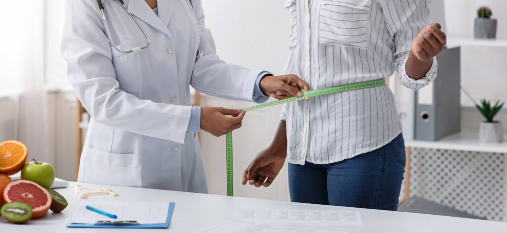 Doctor measuring the waist of a patient, checking progress of weight loss despite resistance