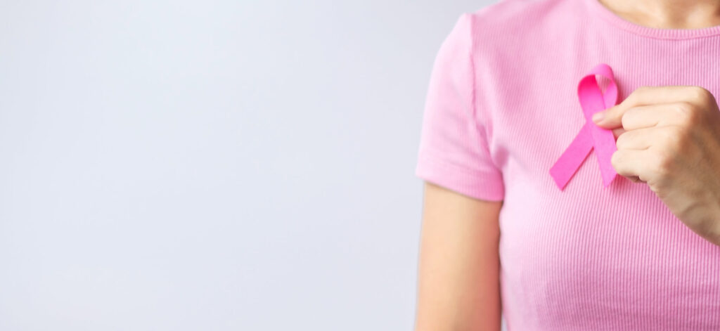 Woman standing, holding a breast cancer ribbon over her chest. Raising awareness of HR+/HER2- breast cancer
