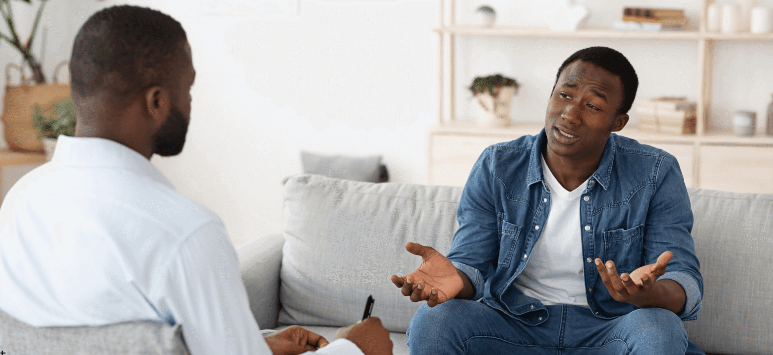 black man (therapist concept) in white shirt talking to a black man patient in blue jacket