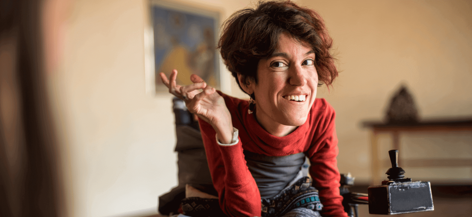 woman wearing a red long sleeve shirt and overalls in wheelchair smiling