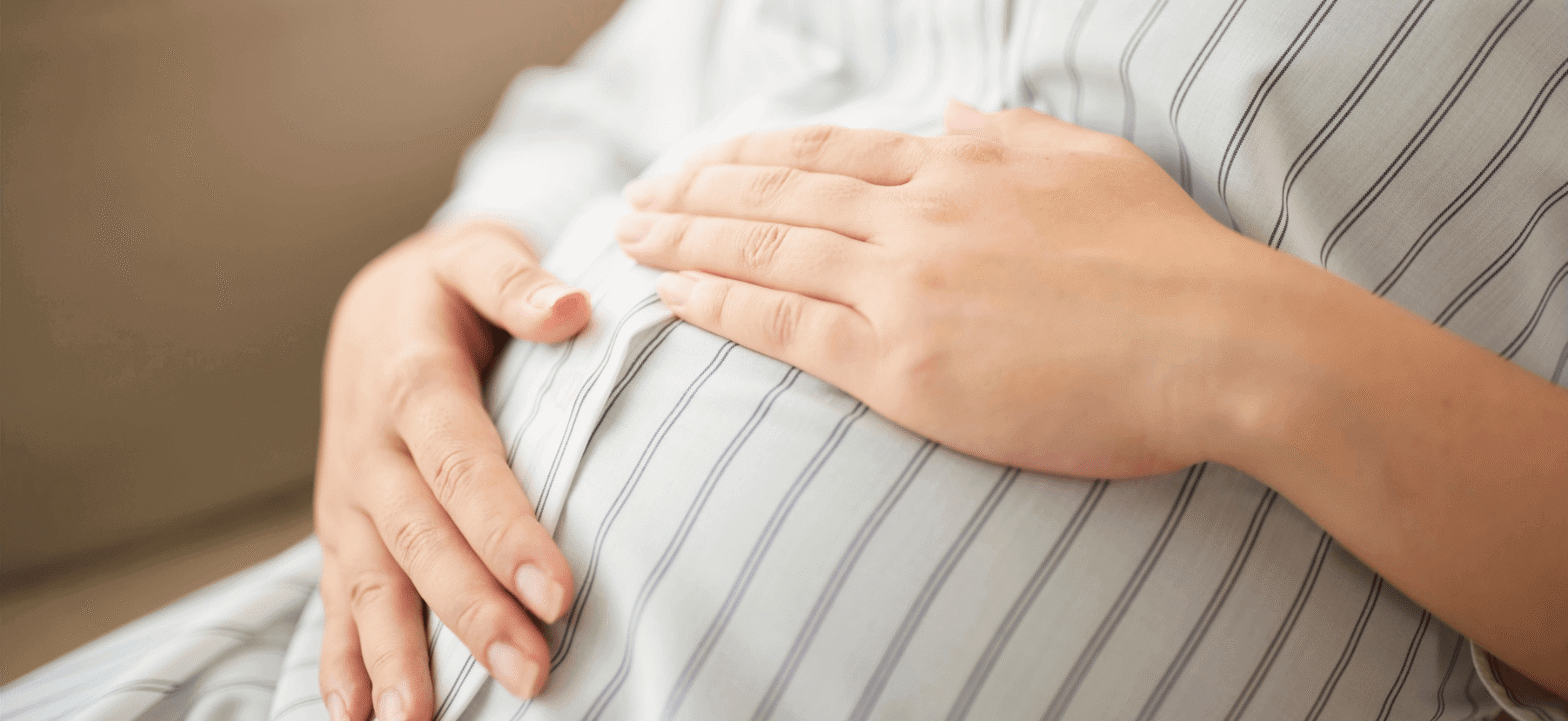 woman touching her baby bump with both hands, wearing a white dress with black thin stripes